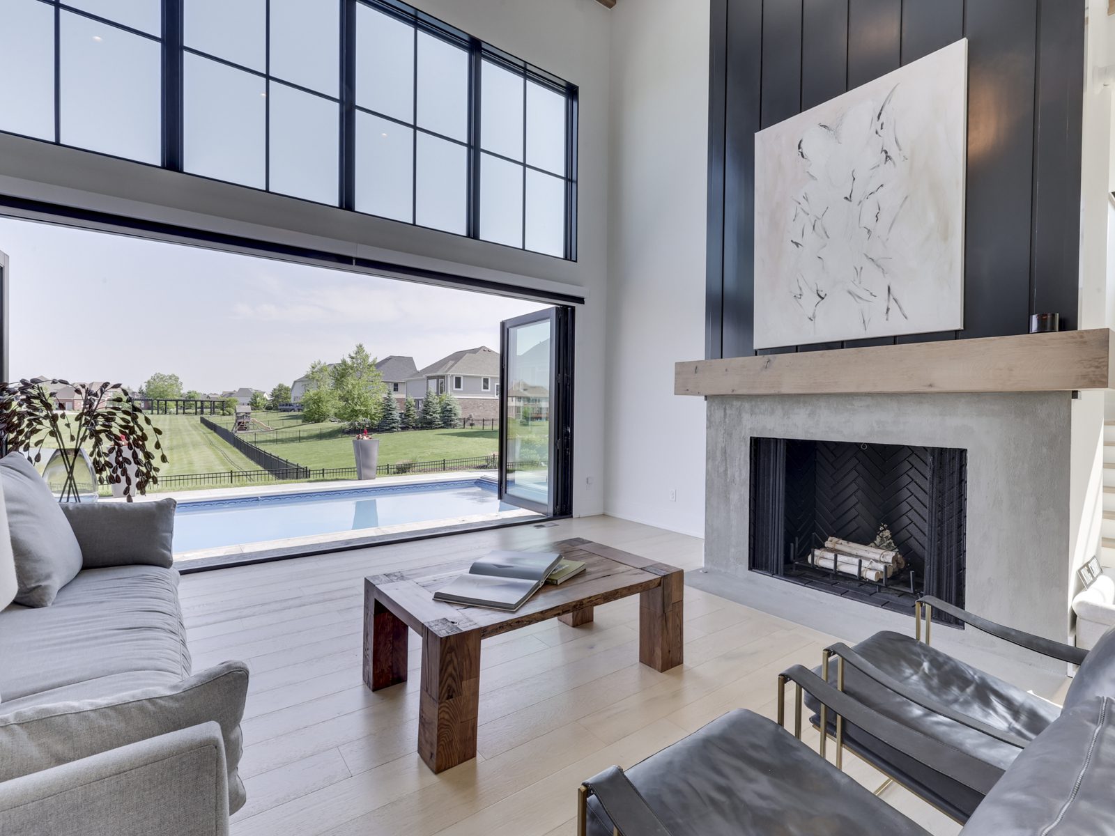 Modern living room featuring large windows that open to a pool view, complemented by a minimalist fireplace and stylish furniture.