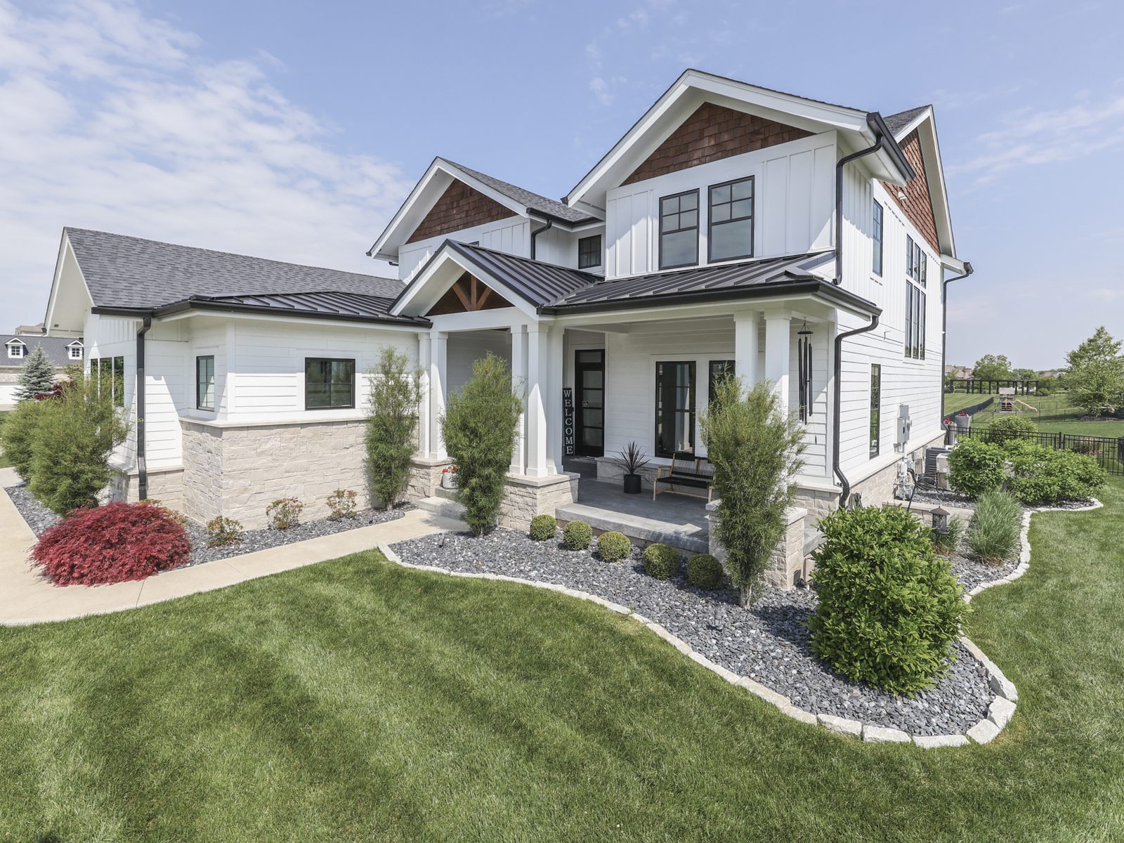 Modern two-story home with a well-manicured yard, featuring a welcoming porch and landscaped gardens. Ideal for showcasing contemporary architecture.